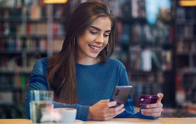 Woman smiling while holding a credit card for purchases on her phone